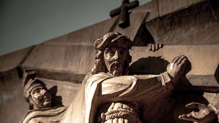 Die Statue eines Mannes mit Bart und Kopfbedeckung vor einem Gebäude mit Kreuz.