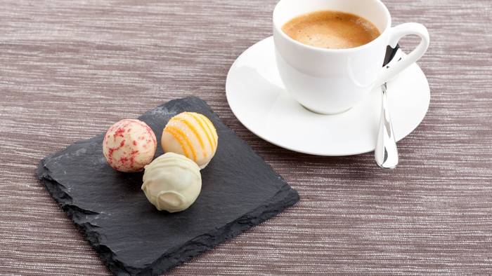 En kaffe i tæppe og tre bonbons på en stenplate