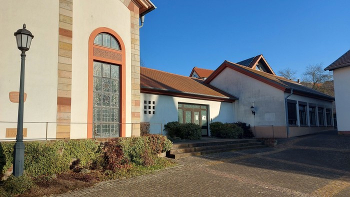Modernes Gebäude mit bogenförmigem Buntglasfenster und angrenzenden weißen Außenwänden unter klarem blauem Himmel.
