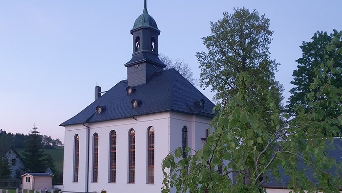 Kirche mit Friedhof und Bäumen im Hintergrund