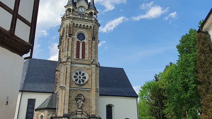 Kirchturm mit Uhr und Kreuzigungsgruppe vor weißem Gebäude
