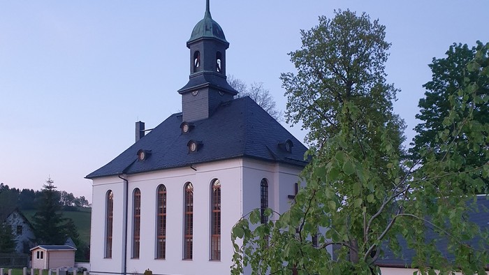 Kirche mit Friedhof und Bäumen im Hintergrund