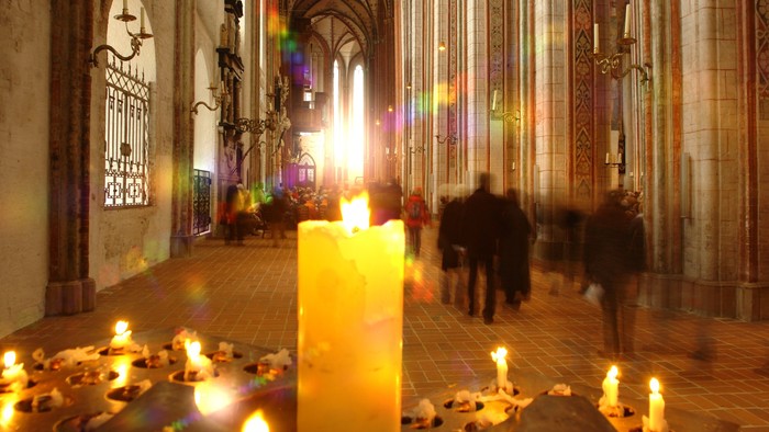 In der Kirche brennen viele Kerzen, Menschen gehen vorbei