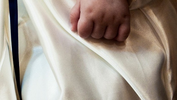 Et lillebitte hånd stikker frem under et blødt, lysebrunt tæppe.