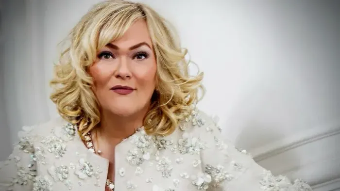 Elegant kvinde i en glitrende hvid jakke med blonde krøller og diskret makeup.