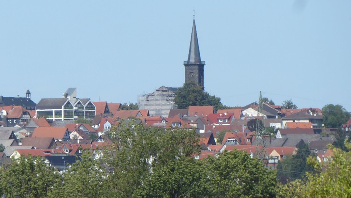Idyllisches Städtchen mit roten Hausdächern und einem markanten Kirchturm, der sich über üppiges Grün erhebt.