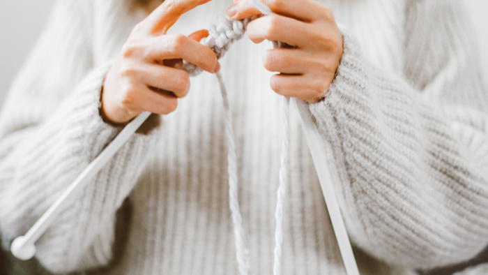 En person spinder med håndspind i hvid trøje.