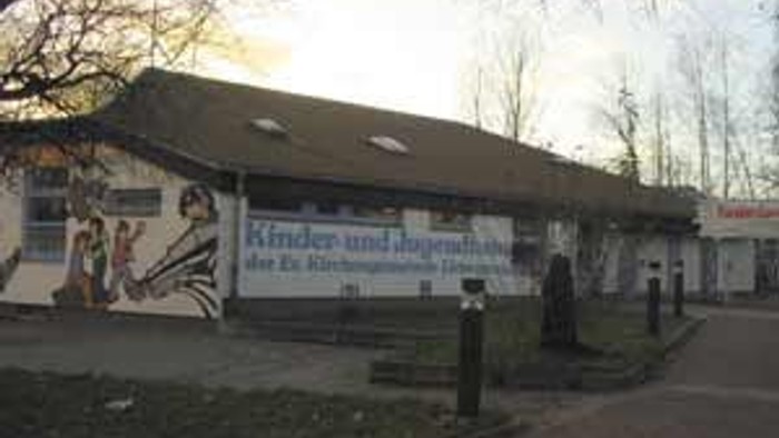 Ein Gebäude mit Wandmalerei mit der Aufschrift „Kinder und Jugendhaus“ in einer parkähnlichen Umgebung während des Sonnenuntergangs.