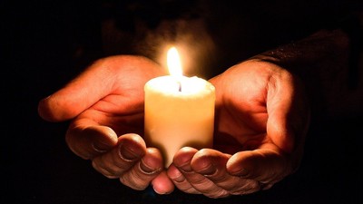 Hands gently holding a lit candle, creating a warm glow.