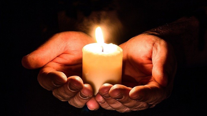 Hands gently holding a lit candle, creating a warm glow.