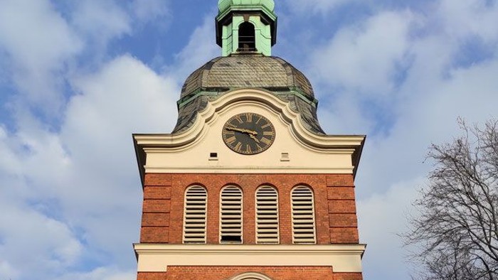 Das Bild zeigt einen Kirchturm mit Uhr und grünem Dach.