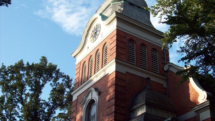 Das Bild zeigt einen Ziegelbau mit Uhrturm und grünem Dach.