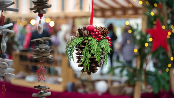 Handgefertigte Festtagskränze und Tannenzapfendekorationen, die an einem festlichen Marktstand hängen.