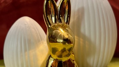 Goldene hasenförmige Parfümflasche, umgeben von weißen Ostereiern.