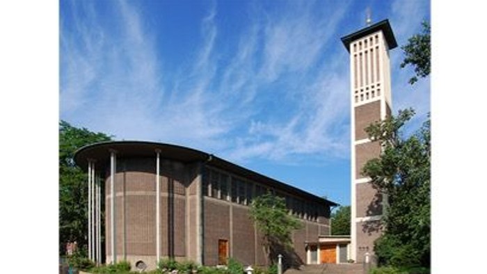 Moderner Kirchenbau mit hohem Glockenturm und geschwungener Backsteinfassade unter klarem Himmel.