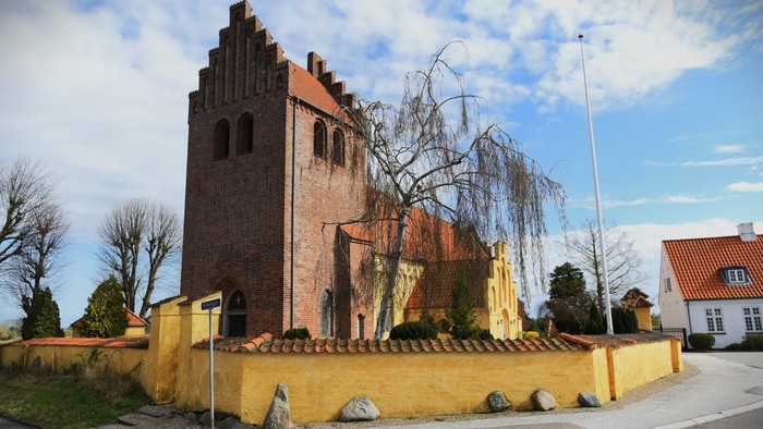 Gul mur og mørkt teglsteins tårn ved vejskæring