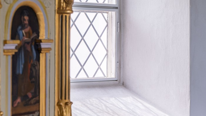 En del af en prægtig, guldfarvet altertavle med malerier ved et vindue i en kirke.