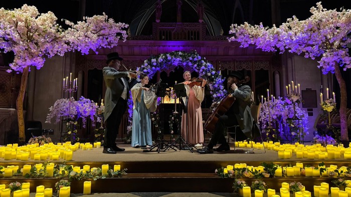 Elegant stage performance with musicians and singers surrounded by floral arches and candlelit arrangements.