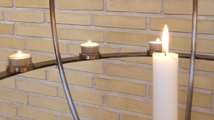 Moderne metalvæglys med tændte stearinlys på en murstensbaggrund.
