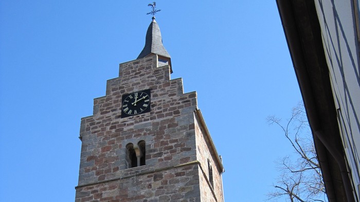 Außenansicht der evangelischen Kirche in Niederelsungen mit hohem Natursteinturm, gestufter Giebelzone und spitzer Dachhaube. 