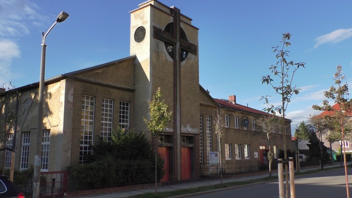 Historisches Backsteingebäude mit Uhrturm und Industrie-Stil-Fenstern an einer sonnigen Straße.