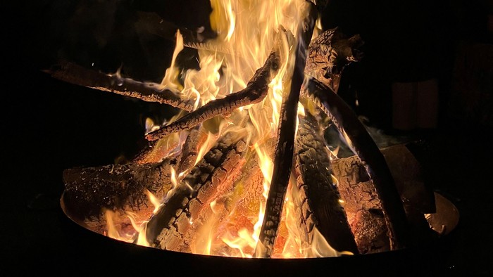 Lebhafte Lagerfeuerflammen beleuchten Holzscheite in einer dunklen Nacht.