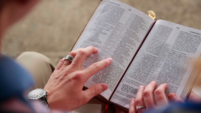 Person, die eine geöffnete Bibel liest, mit den Händen auf den Seiten ruhend.