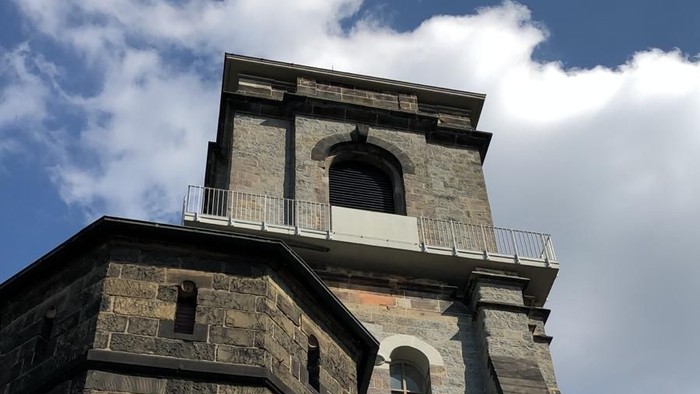 Historischer Steinkirchturm mit Bogenfenstern und einem Glockenbereich unter einem teilweise bewölkten Himmel.