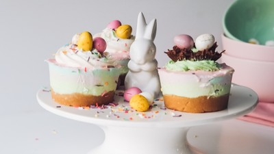 Ein Kuchenständer mit drei Ostertorten, verziert mit bunten Eiern und einem weißen Osterhasen.