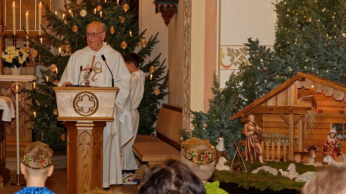 Ein Priester predigt an einem Pult in einer festlich geschmückten Kirche.
