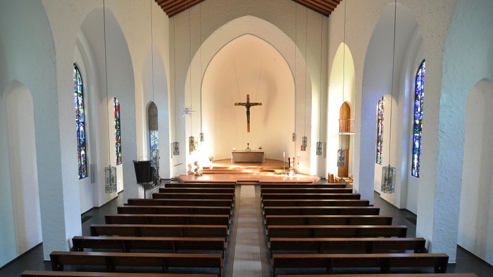 Moderne Kircheninnenausstattung mit hölzernen Kirchenbänken, Buntglasfenstern und einem zentralen Kruzifix-Altar.