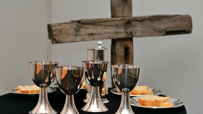 Elegante silberne Kelche und Hostien, arrangiert auf einem Tisch mit einem hölzernen Kreuz im Hintergrund.
