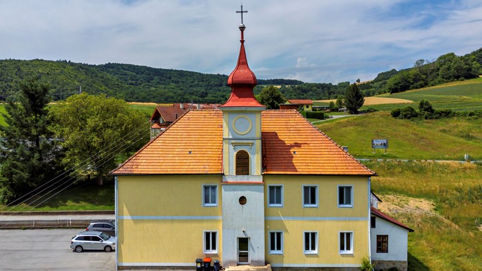 Eine charmante gelbe Kirche mit rotem Turm und Uhr, eingebettet in eine malerische ländliche Landschaft.