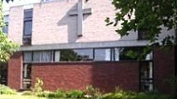 Modernes zweistöckiges Gebäude mit Ziegeluntergeschoss und hell gestalteter oberer Etage, umgeben von Grünflächen.