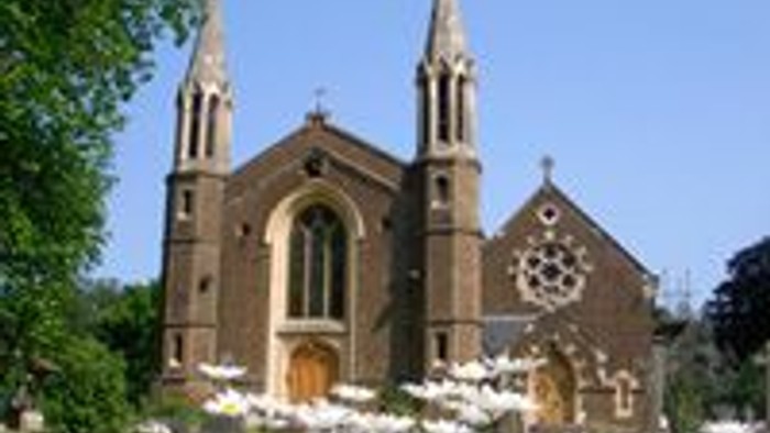 Historische Backsteinkirche mit Zwillingstürmen und bunten Glasfenstern vor einem klaren blauen Himmel.