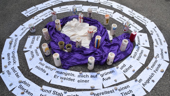 Ein Kreis aus weißen Pappschildern mit deutschen Texten umgibt eine Mitte mit Kerzen und einem Tuch.