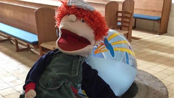 En person med rød hårpuppe sidder på en benk.