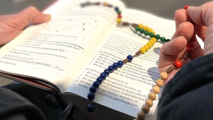 Person hält ein offenes Buch und eine Perlenkette