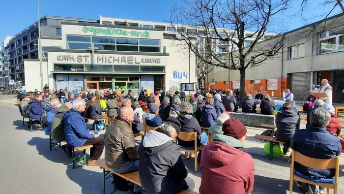 Menschen sitzen im Freien vor einem Gebäude und essen.