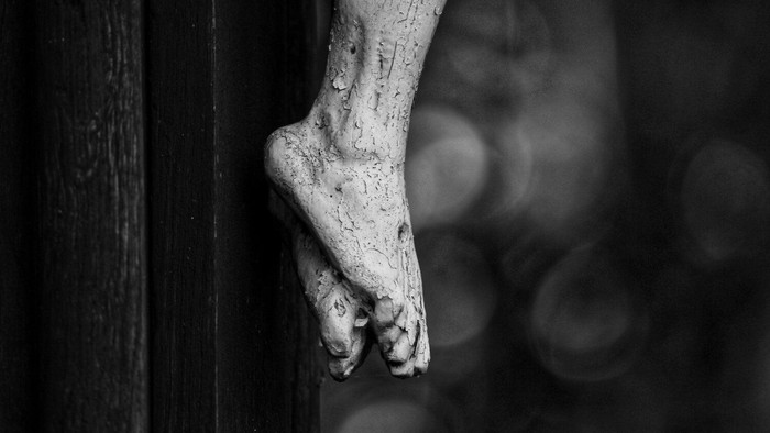 Ein Bein mit sichtbaren Venen und Muskeln lehnt an einer dunklen Holzwand.