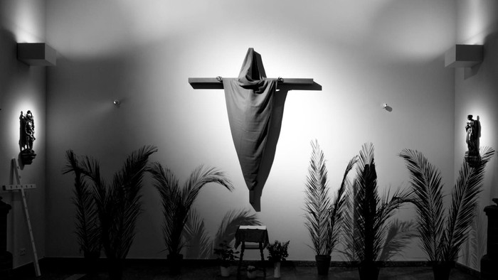 Ein Kreuz mit Tuch in einer Kirche, umgeben von Palmen und Kerzen.