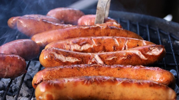 Gegrillte Würstchen, die auf einem heißen Grill brutzeln, mit ein paar Kartoffeln daneben.