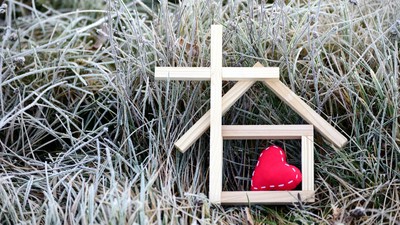 Ein hölzernes Haus mit Herz und Kreuz im gefrorenen Gras.