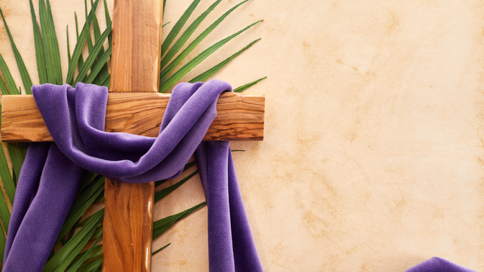 Holzkreuz mit Palmenzweigen und violettem Tuch