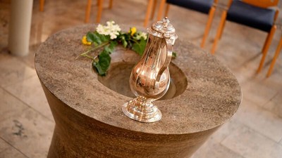 Ein silberner Krug mit Blumen steht auf einem Steintisch.