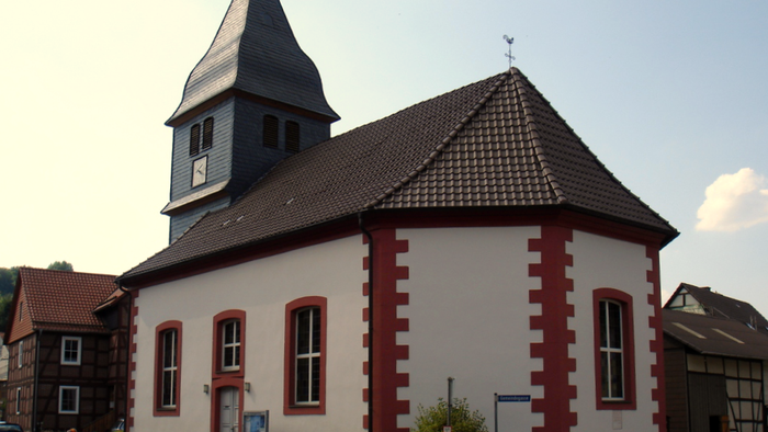 Weißes Gebäude mit roter Umrandung und Turmspitze, umgeben von anderen Gebäuden.
