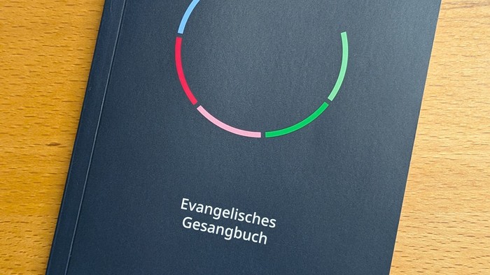 Evangelisches Gesangbuch mit buntem kreisförmigem Logo auf schwarzem Einband.