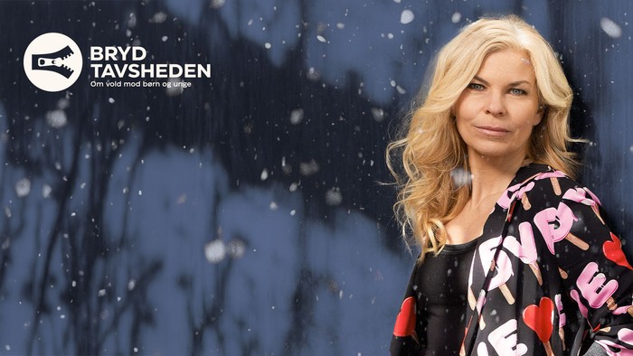 Kvinde i sort jakke med lyserøde hjerter står i faldende sne og promoverer Bryd Tavsheden-kampagnen.