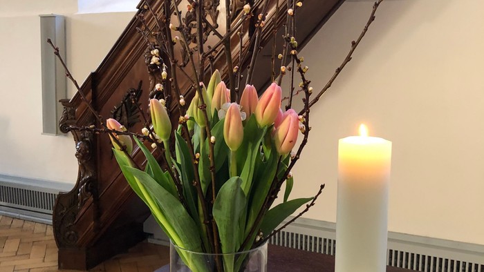Ein Blumenstrauß und eine brennende Kerze stehen auf einem Tisch vor einer Treppe