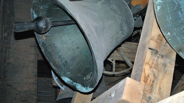 Ein großer, grünlich-brauner Glockenkörper mit einem Klöppel.